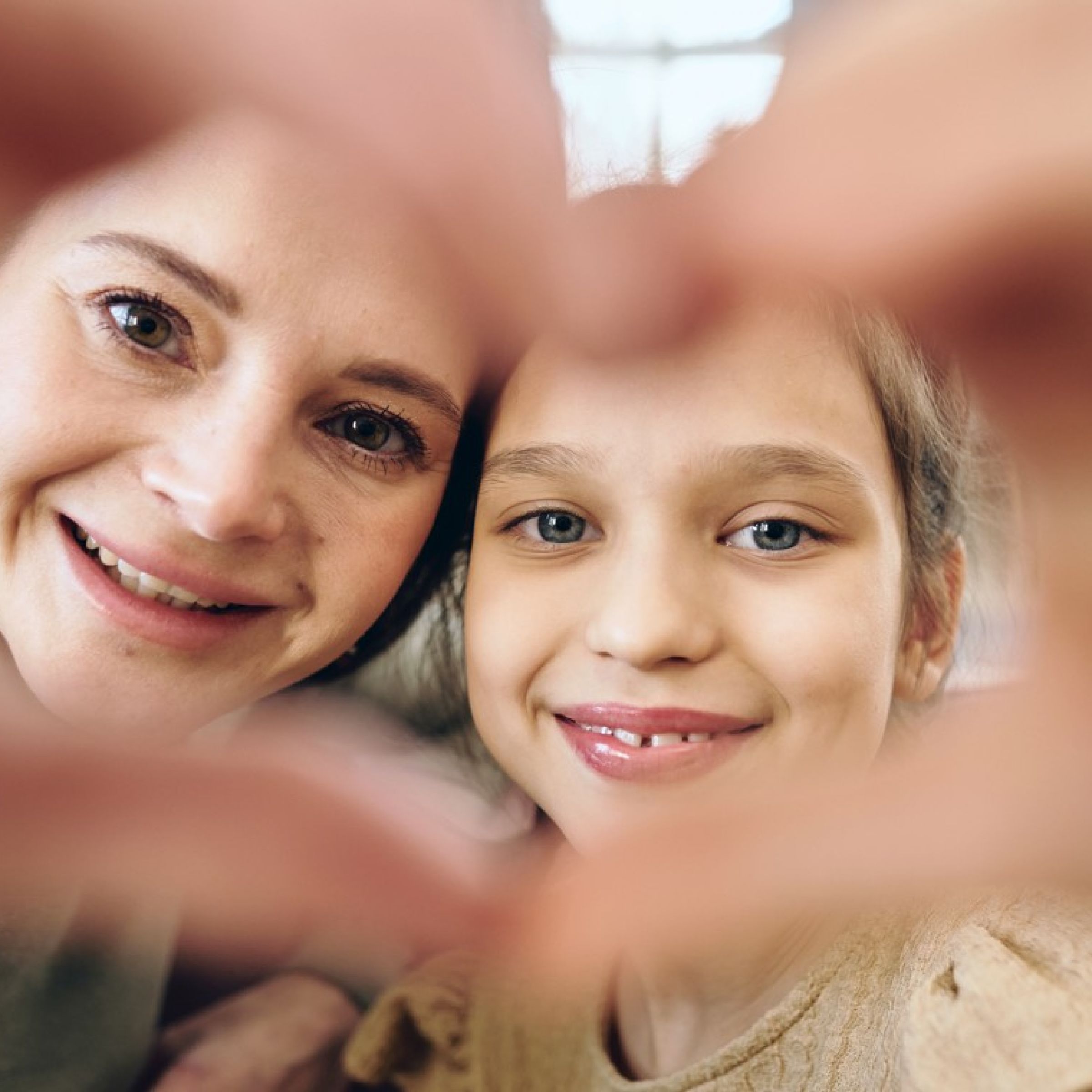 Spenden eine Frau und ein Mädchen bilden mit ihren Händen gemeinsam ein Herz, duch das sie schauen
